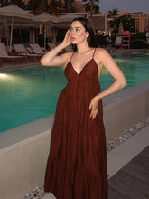 Woman in a brown dress standing by a poolside at night.
